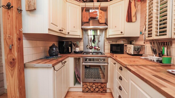 A compact kitchen with white cabinets, a stove, microwave, and various utensils. - Cool Cabin (Leek)