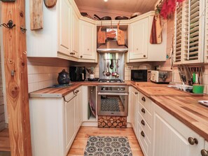 A compact kitchen with white cabinets, a stove, microwave, and various utensils. - Cool Cabin (Leek)
