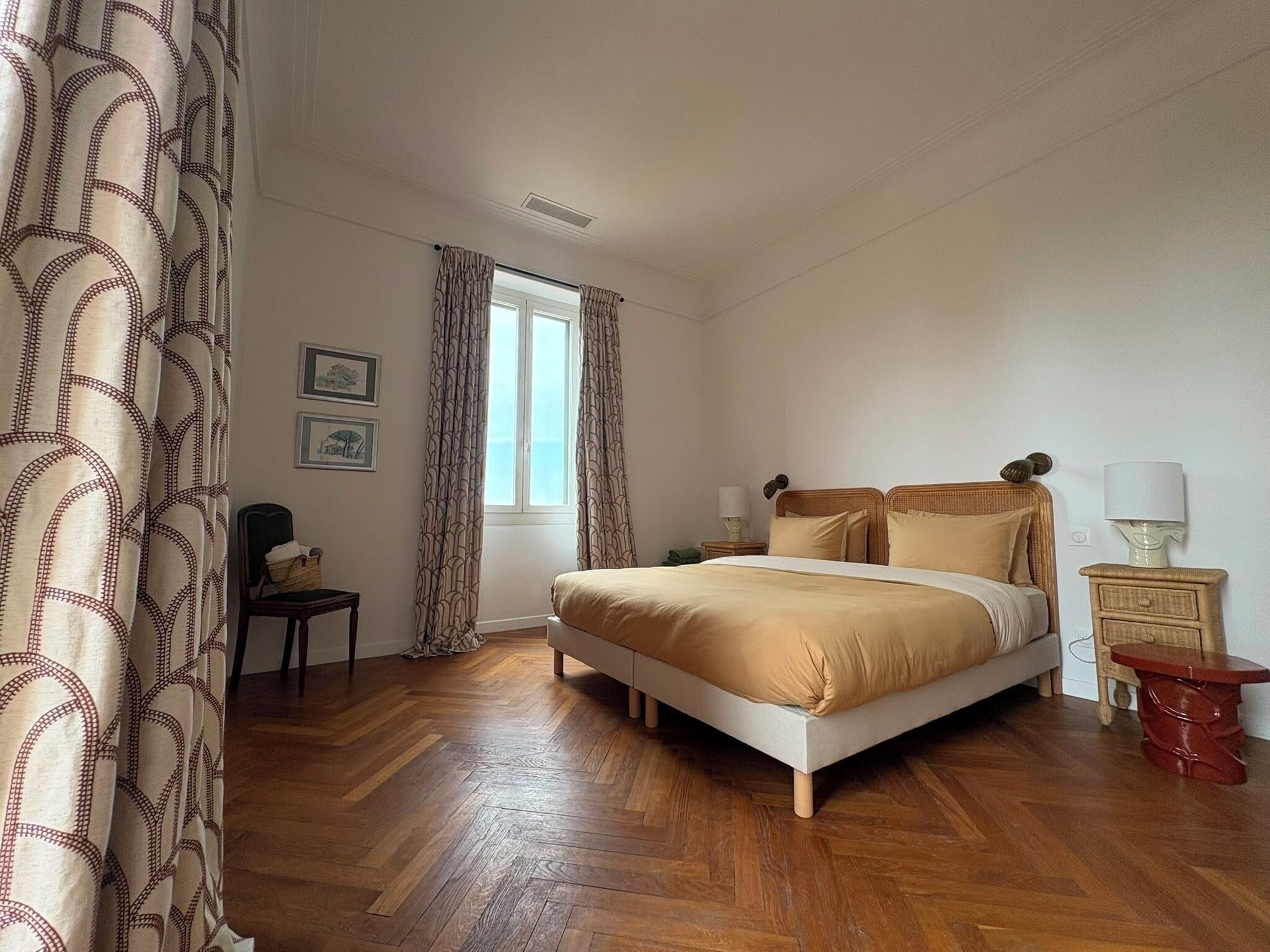 Una habitación de hotel con cama, una silla, una mesita de noche, lámpara y ventana con cortinas.