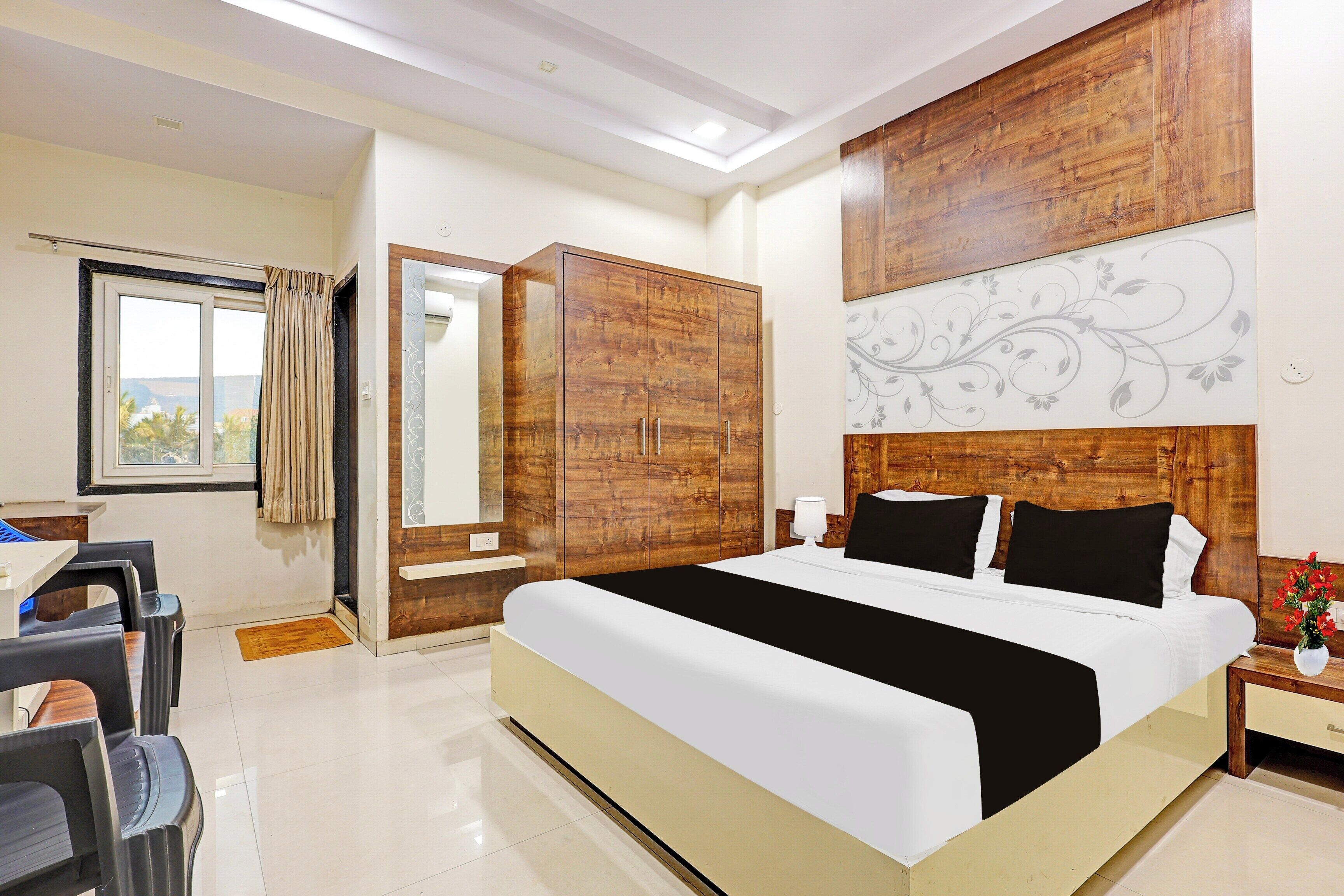 Una camera d'albergo con un letto grande, un armadio in legno, una scrivania con sedie e una finestra con tende.