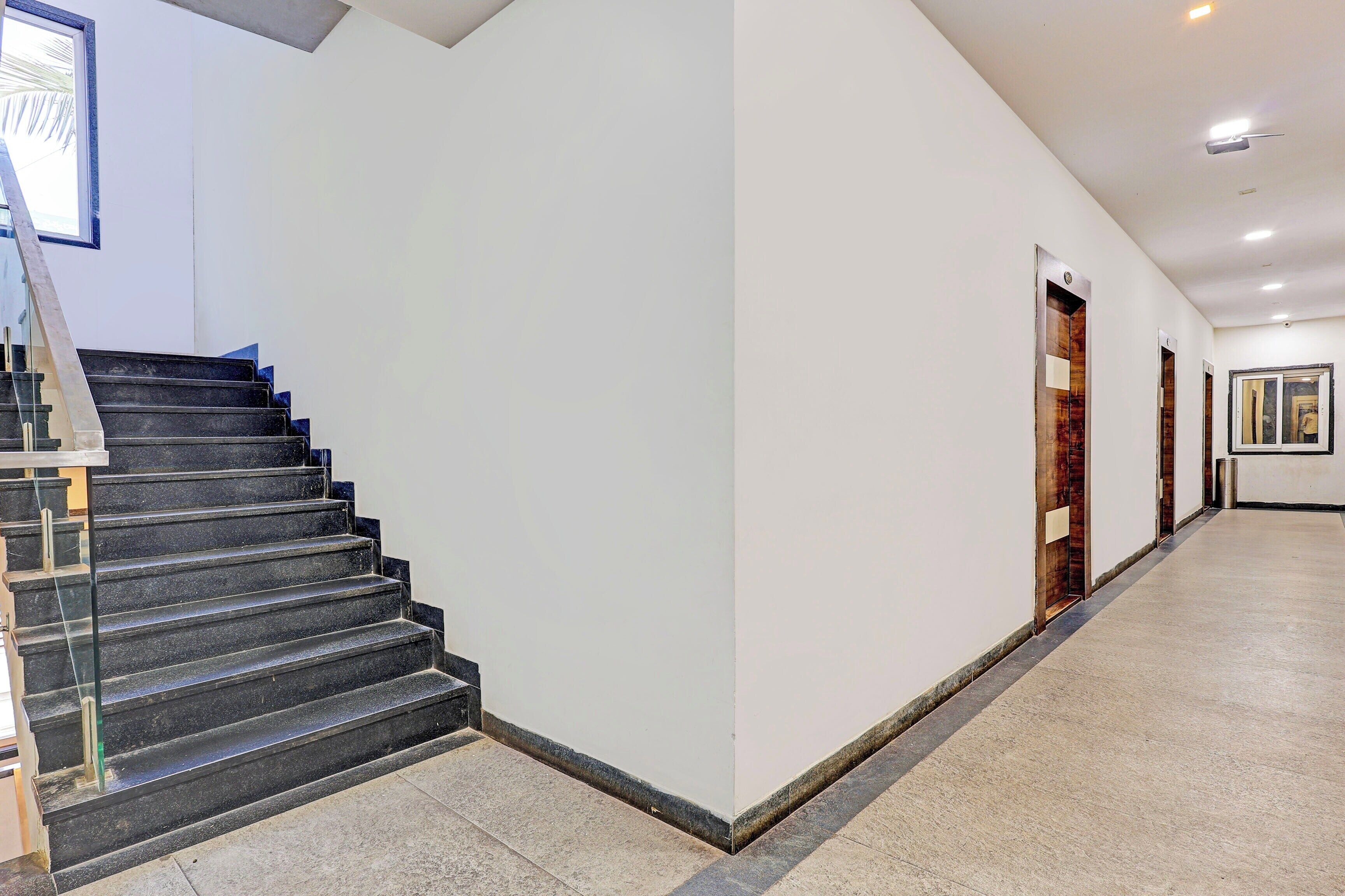 Un couloir avec un escalier menant à l’étage sup érieur, une porte avec un miroir et une poubelle.