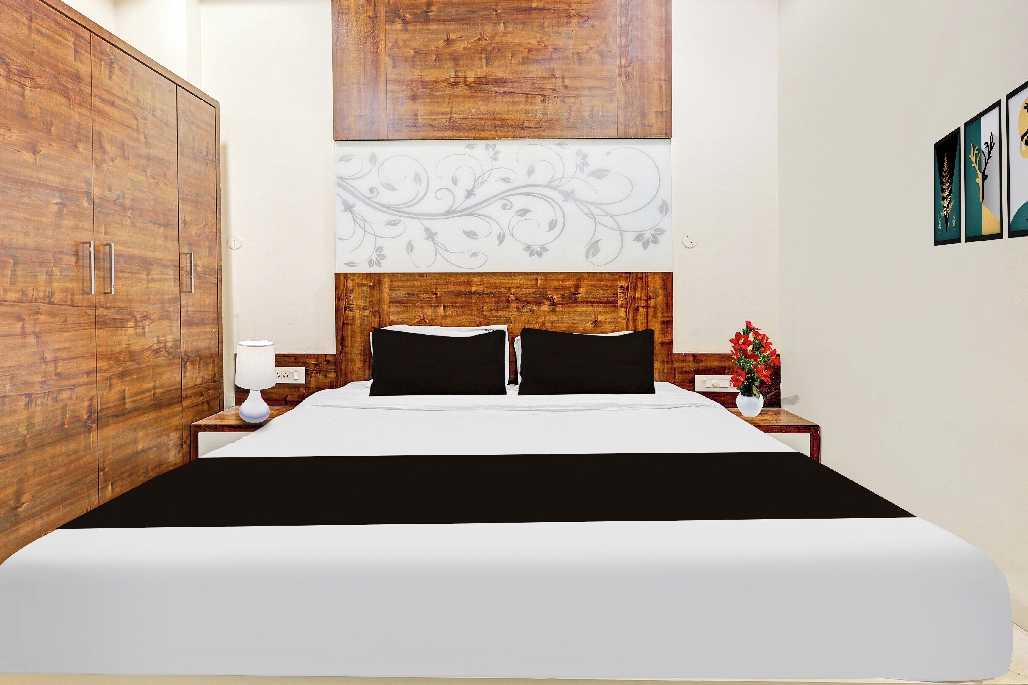Une chambre d’hôtel avec un grand lit, une tête de lit en bois, une table de chevet avec une lampe et un mur orné de tableaux encadrés.