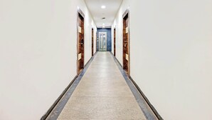 Een lange, smalle hotelgang met betegelde vloer en houten deuren aan beide zijden.