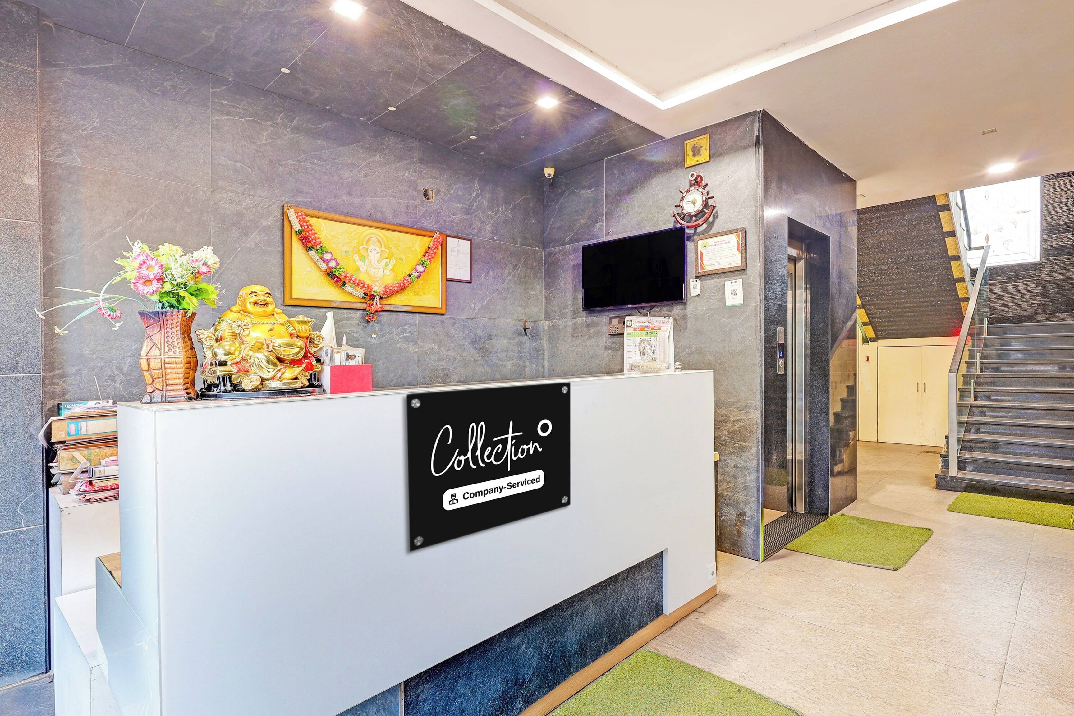Bancada de recepção com placa indicando serviço da empresa, um quadro com imagem de uma divindade, um relógio e um elevador.