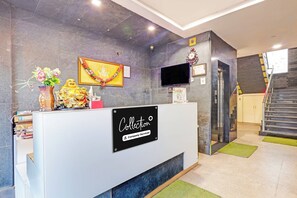A reception desk with a sign indicating it's company-serviced, a framed picture of a deity, a clock, and an elevator. - Super OYO Collection O Vizag (Visakhapatnam)