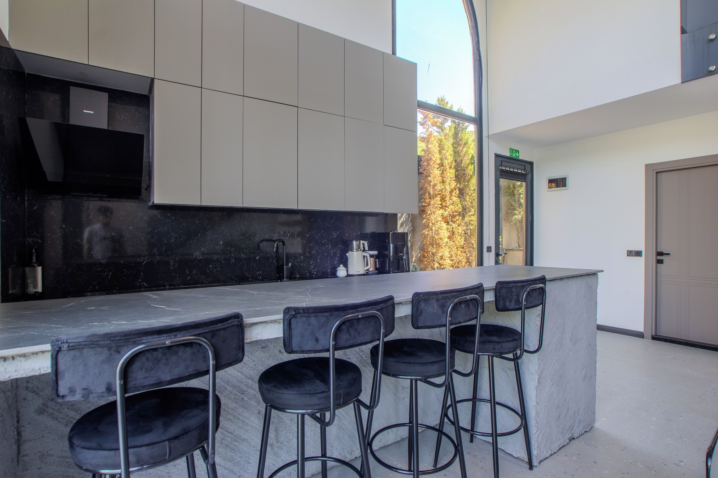 Una cocina moderna con barra, taburetes de bar y vista a árboles fuera.