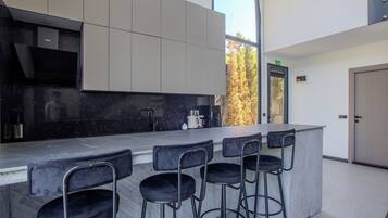 Una cocina moderna con barra, taburetes de bar y vista a árboles fuera.