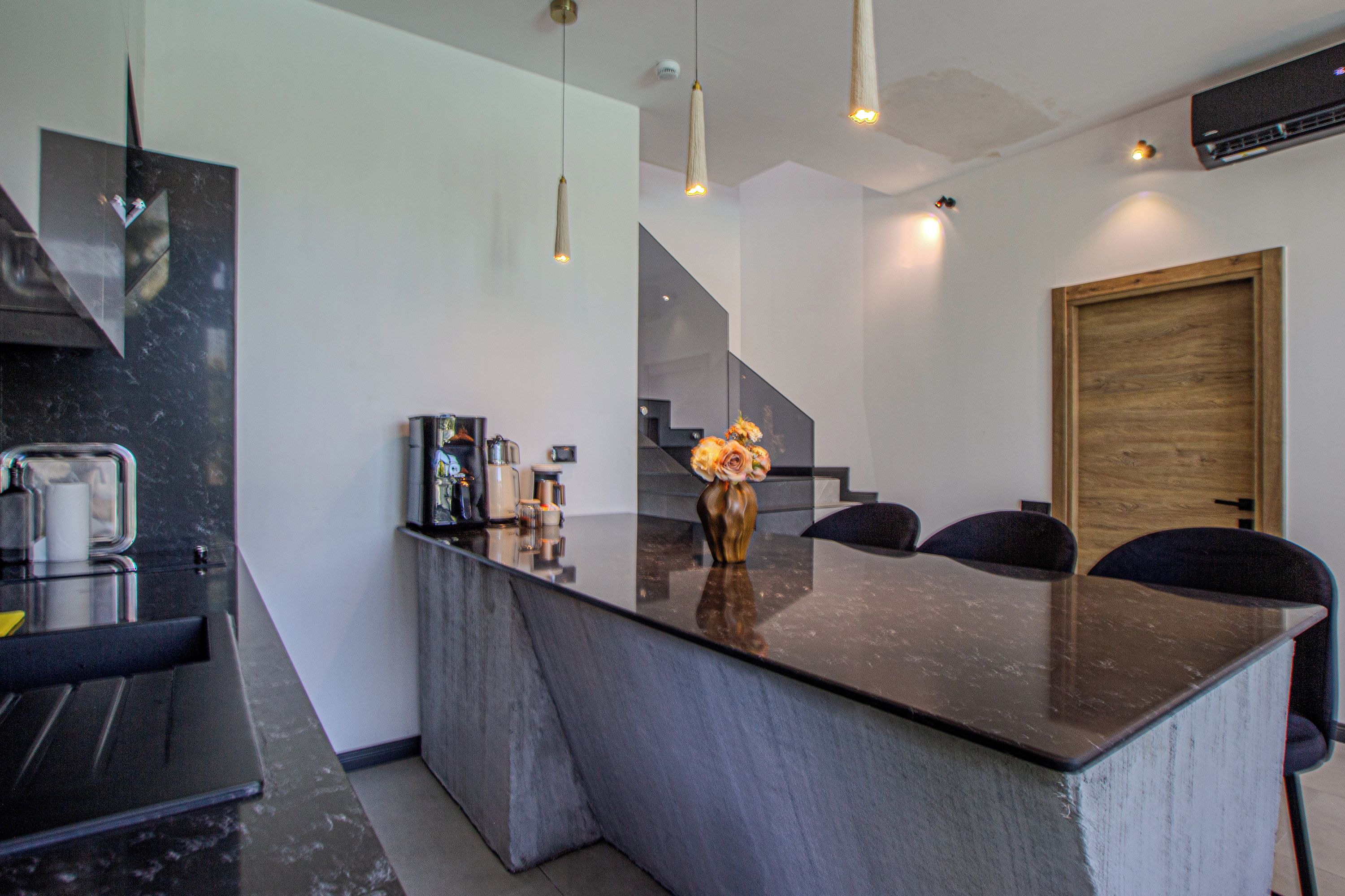 Una cocina moderna con una isla central, iluminación colgante y una puerta de madera.