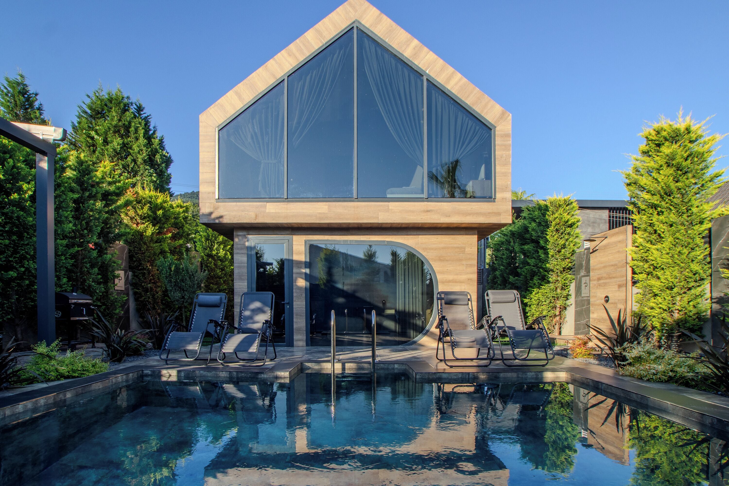 A modern house with a large glass window, a swimming pool, and outdoor seating.