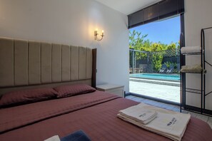 Une chambre à coucher comprenant un lit, une table de chevet, une lampe fixée au mur et donnant sur une piscine extérieure.