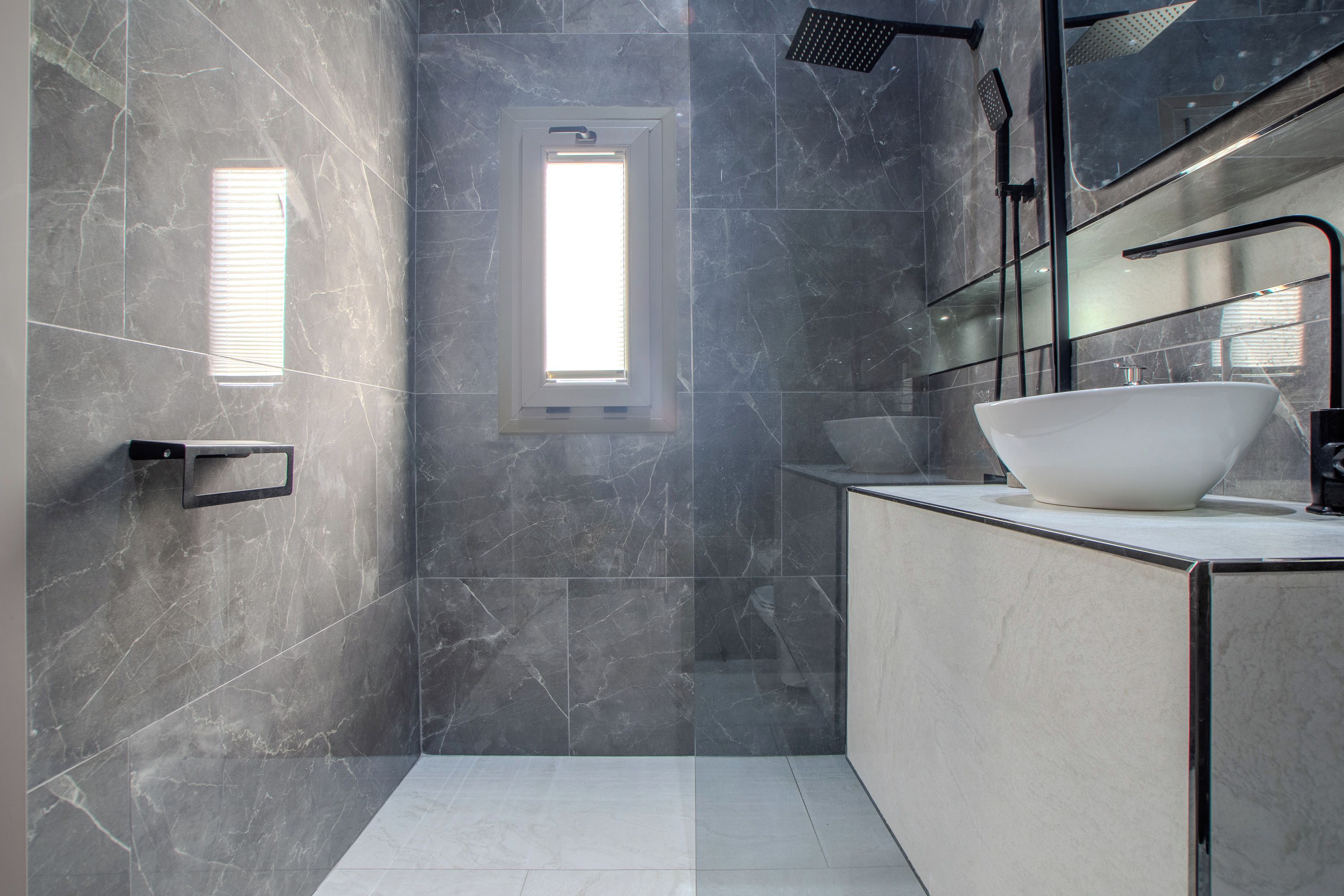 A modern bathroom with a large white sink, a mirror, and a shower.