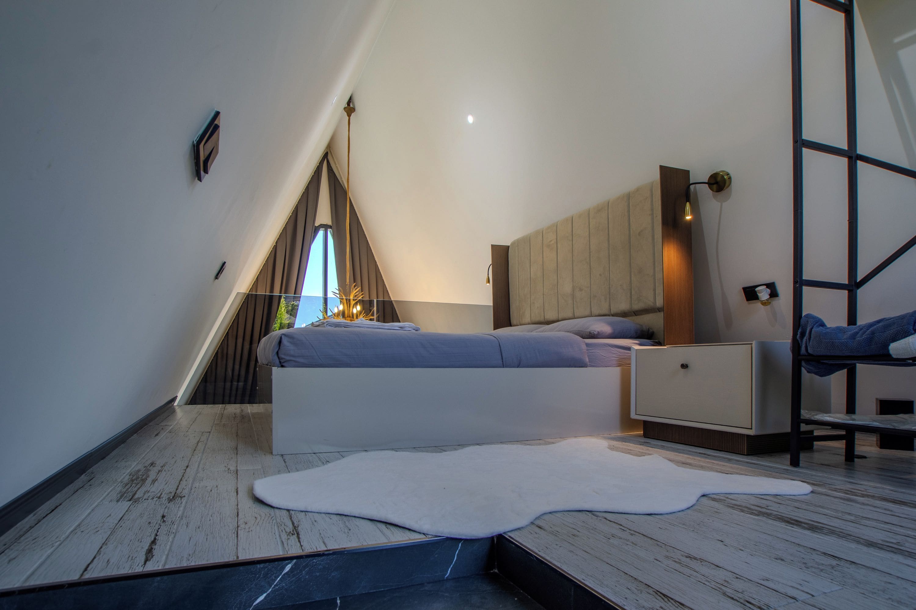 A modern bedroom with a sloped ceiling, a bed, a nightstand, and a large window.