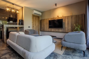 A modern living room with a sectional sofa, a flat-screen TV mounted on a wooden wall, and a coffee maker on the counter.
