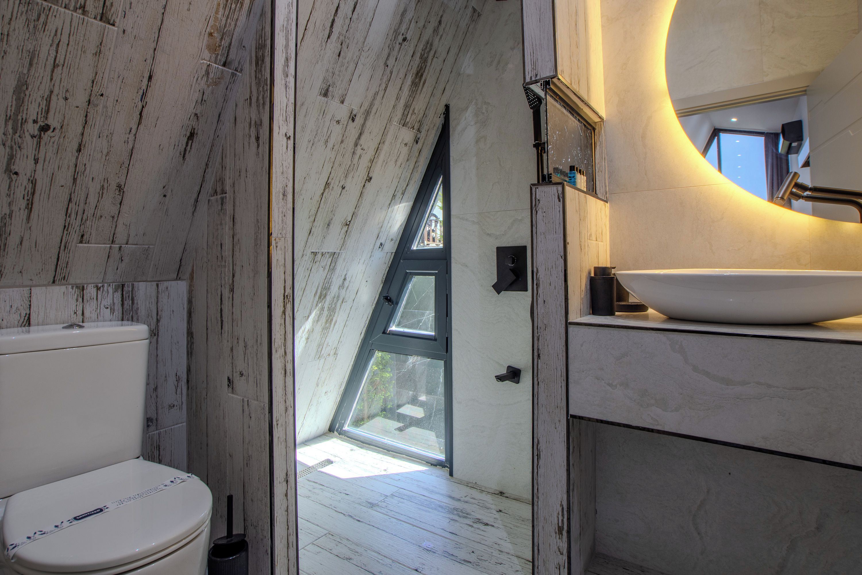 A bathroom with a white toilet, a large oval sink, and a skylight.