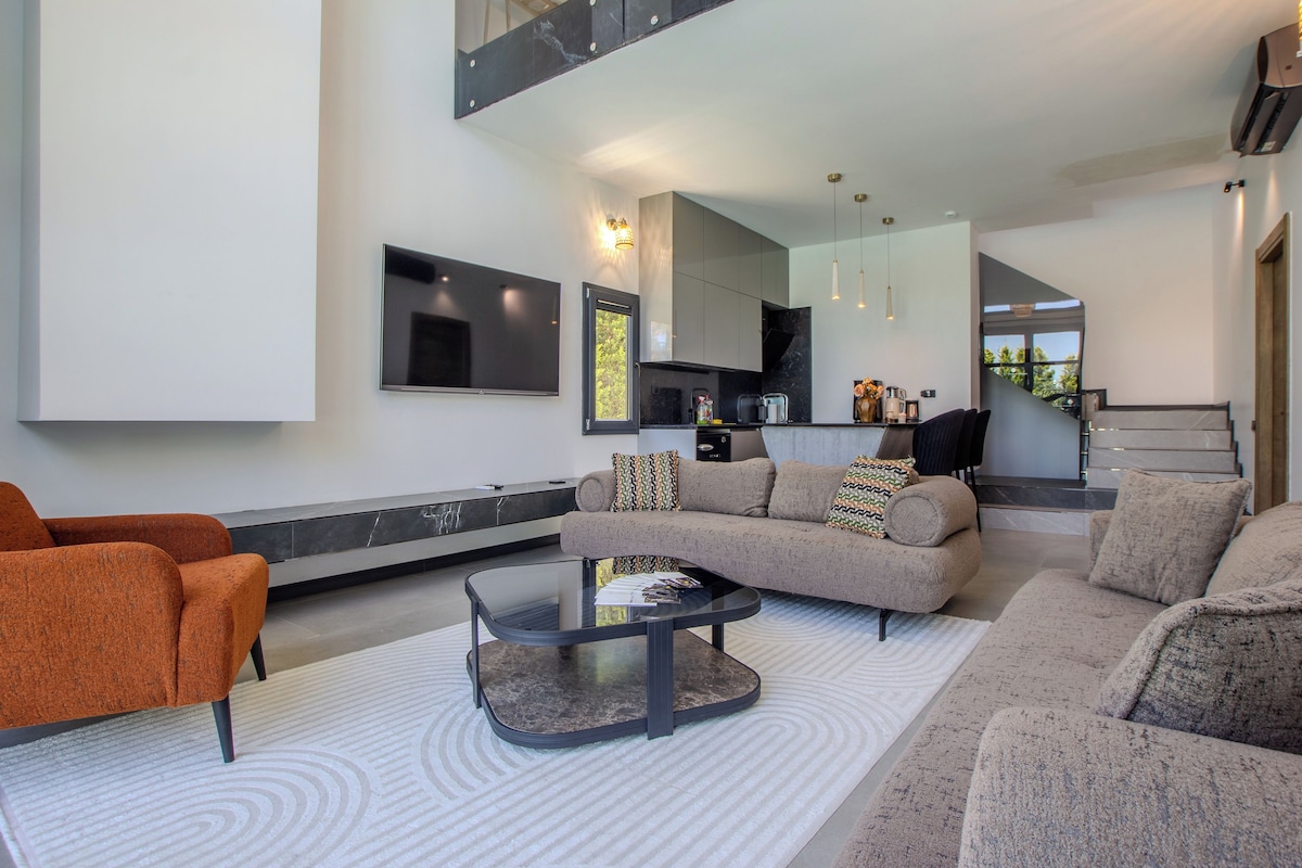 A modern living room with a sectional sofa, a coffee table, and a flat-screen TV mounted on the wall.