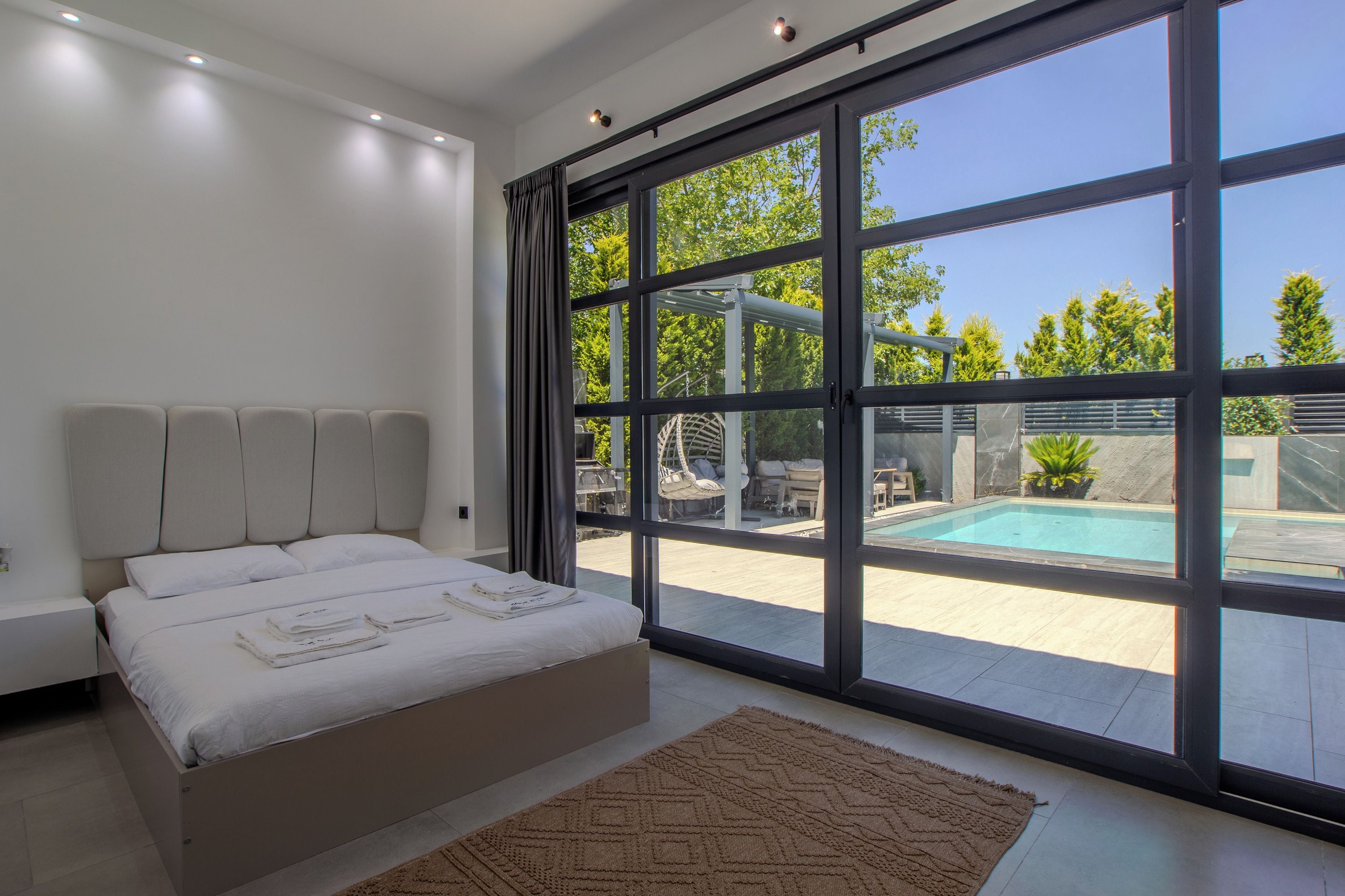 Un dormitorio moderno con una cama grande, vista a una piscina y puerta de vidrio que da al exterior.