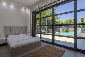 Un dormitorio moderno con una cama grande, vista a una piscina y puerta de vidrio que da al exterior.
