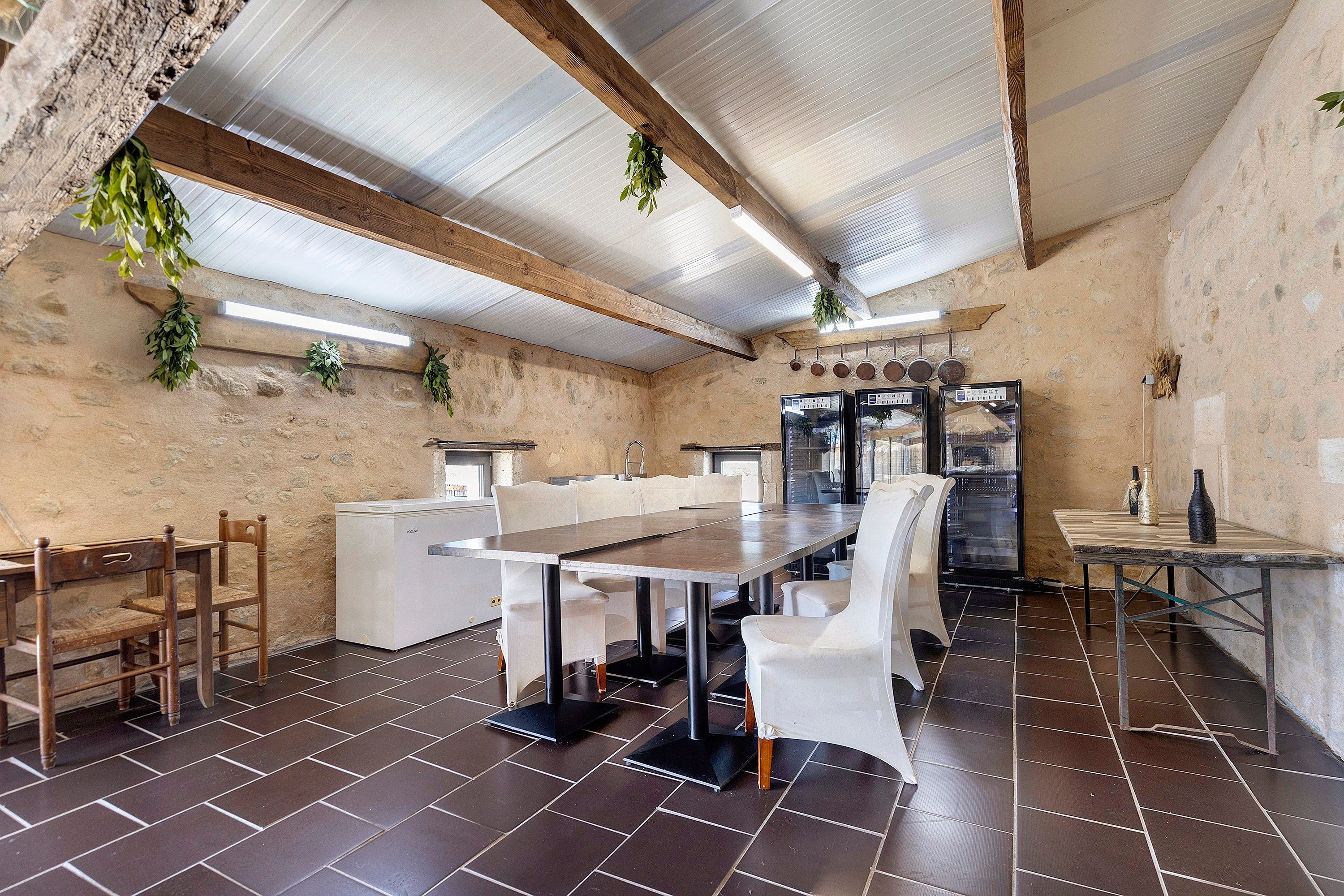 A rustic dining area with a long table, white chairs, and a refrigerator.