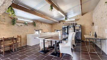 A rustic dining area with a long table, white chairs, and a refrigerator.