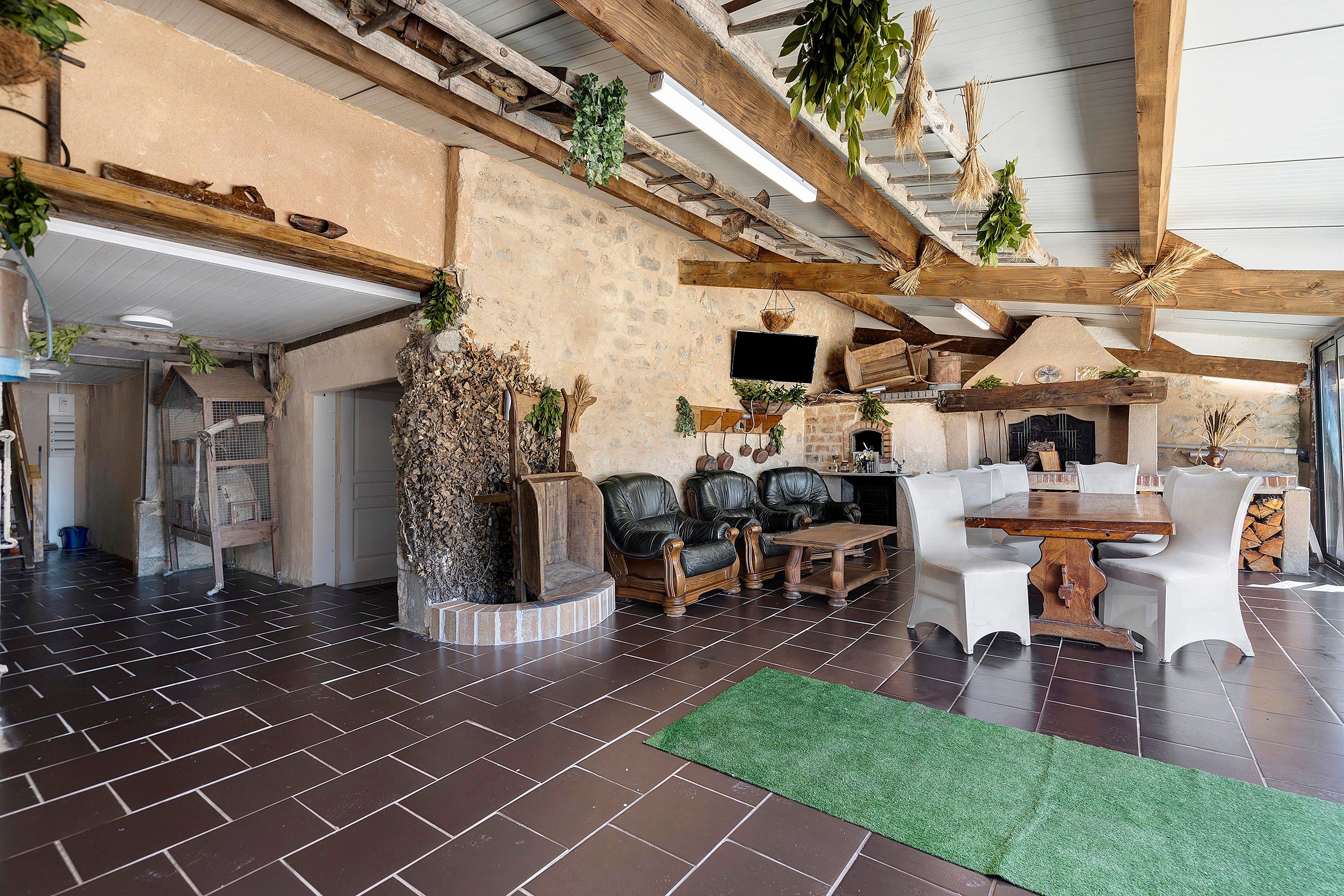 Ein rustikales Interieur mit freiliegenden Holzbalken, einem Kamin aus Naturstein, Ledersofas und einem grünen Teppich aus Kunstrasen.