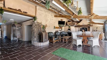 A rustic interior with exposed wooden beams, a stone fireplace, leather sofas, and a green artificial turf rug.