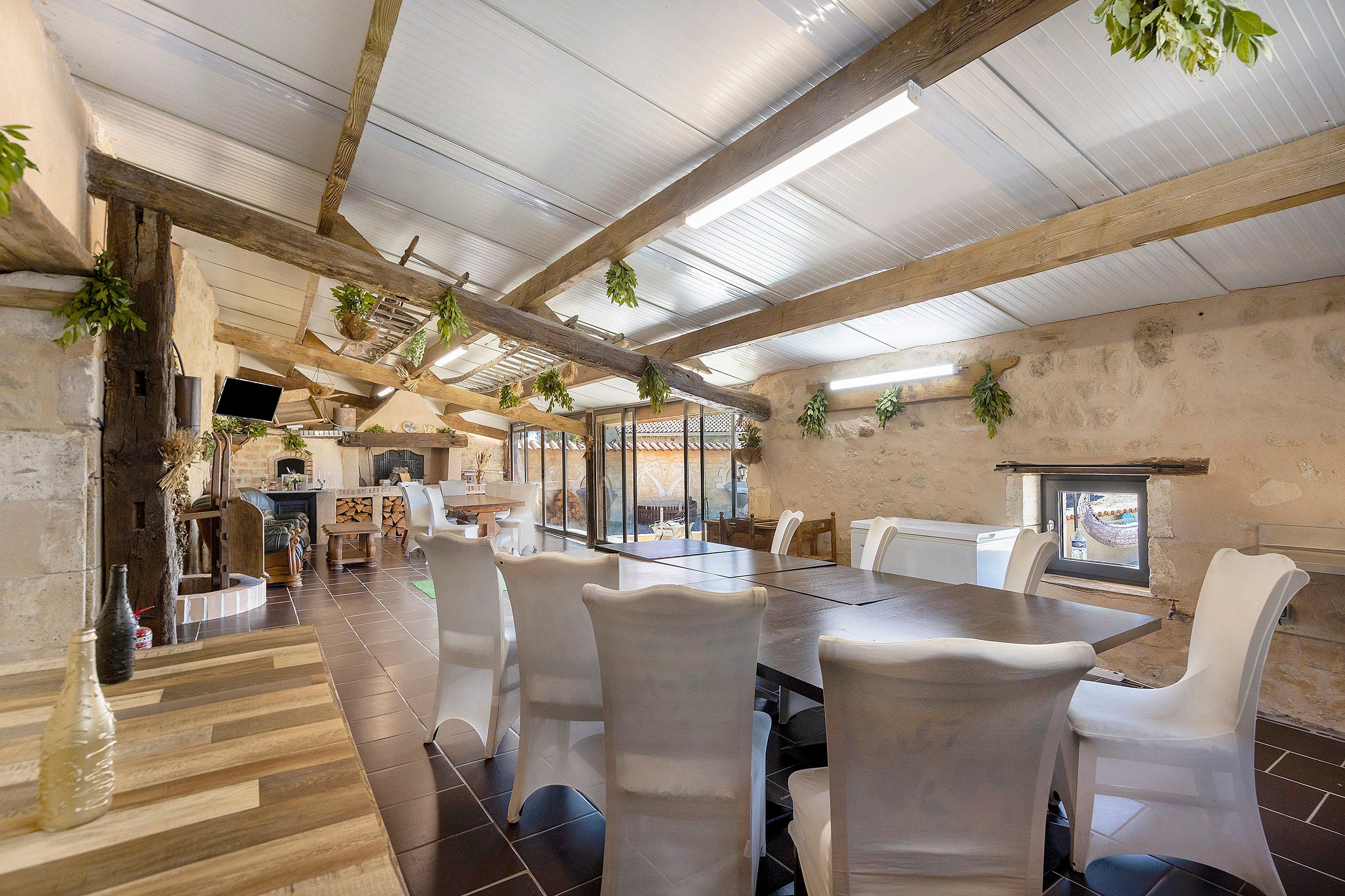 A spacious dining area with a long table, white chairs, and hanging plants.