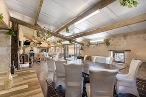 A spacious dining area with a long table, white chairs, and hanging plants.