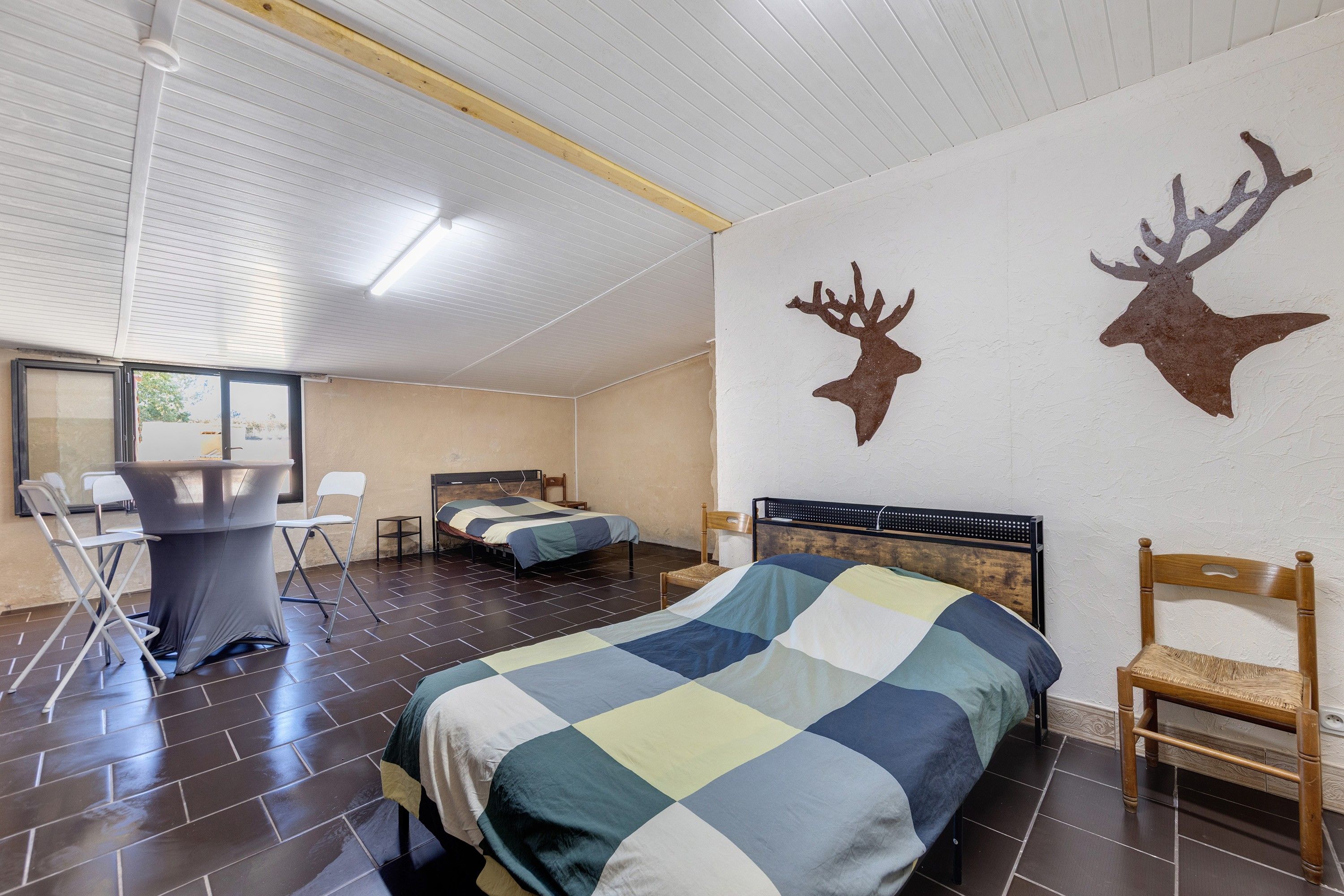 A bedroom with two beds, a desk, chairs, and two mounted deer head decorations on the wall.