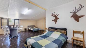A bedroom with two beds, a desk, chairs, and two mounted deer head decorations on the wall.