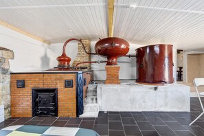A room with a brick fireplace, a large copper boiler, and a black door.
