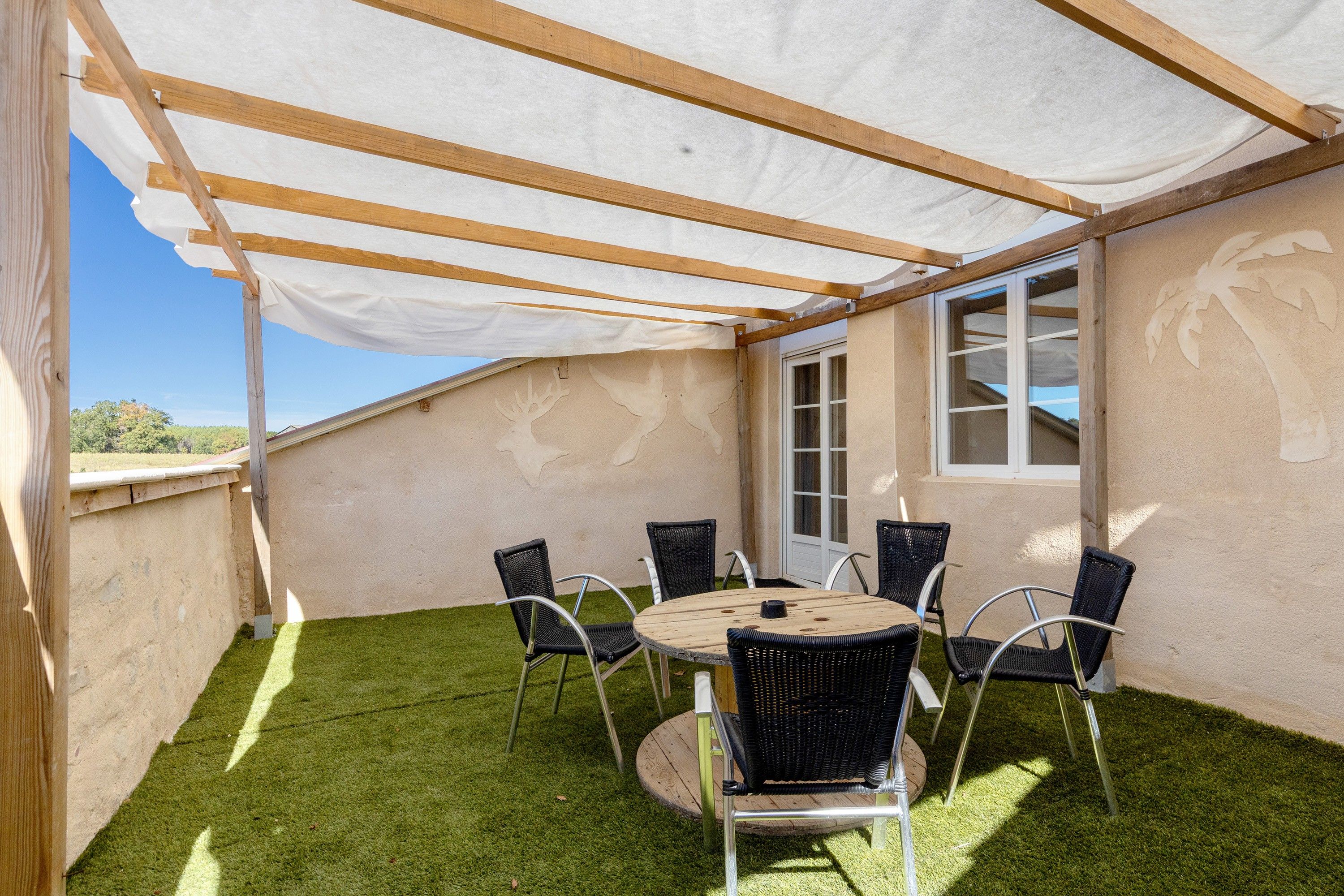Une terrasse couverte avec une table et des chaises, une porte et une vue sur le ciel.