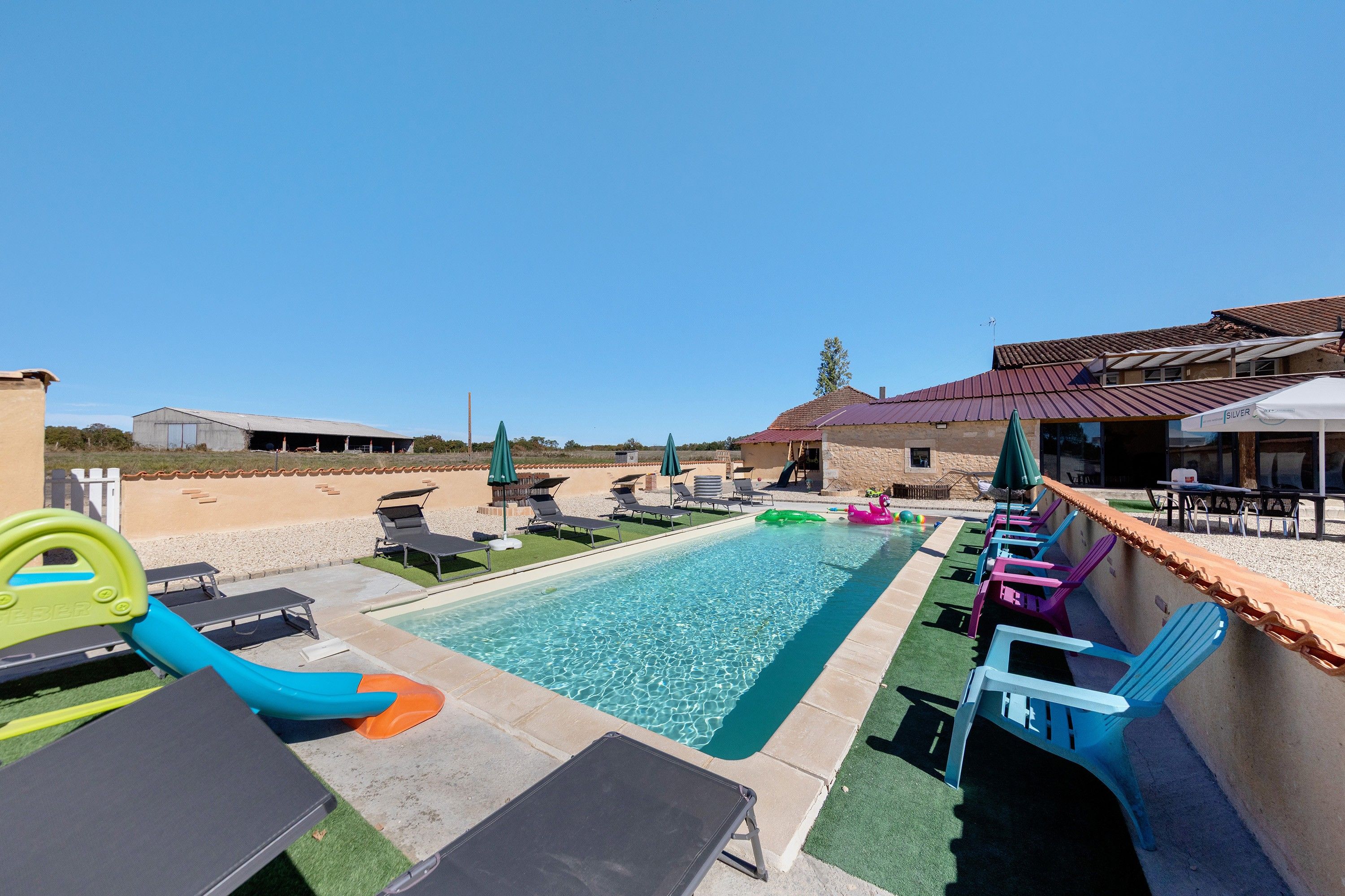 A swimming pool with lounge chairs and a slide, surrounded by a patio area with umbrellas.