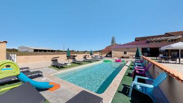A swimming pool with lounge chairs and a slide, surrounded by a patio area with umbrellas.