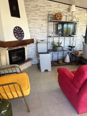 A living room with a fireplace, a clock, a television, and a red armchair.