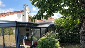 A conservatory with a glass roof, a white wall, and a red-tiled roof visible in the background.