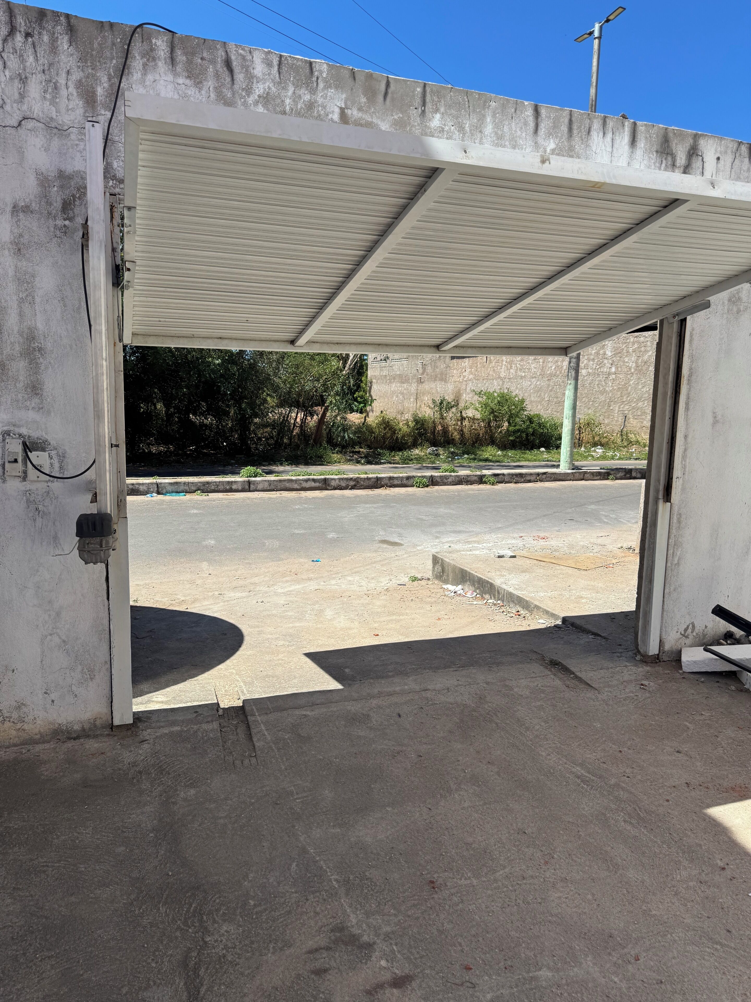 Ett garage utan väggar, med ett betonggolv, ett tak av metall och en delvis synlig vägg med en elcentral.