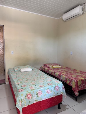 Una habitación con dos camas, cada una con una colcha de flores, falda roja para la cama y una toalla blanca en una de ellas. Un equipo de aire acondicionado está montado en la pared.