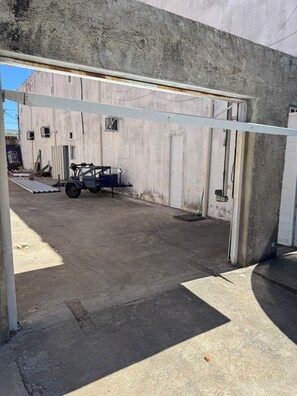 A concrete building with a garage door, a blue utility vehicle, and a small window. - HOTEL POUSADA JESUS ME DEU (Iguatu)