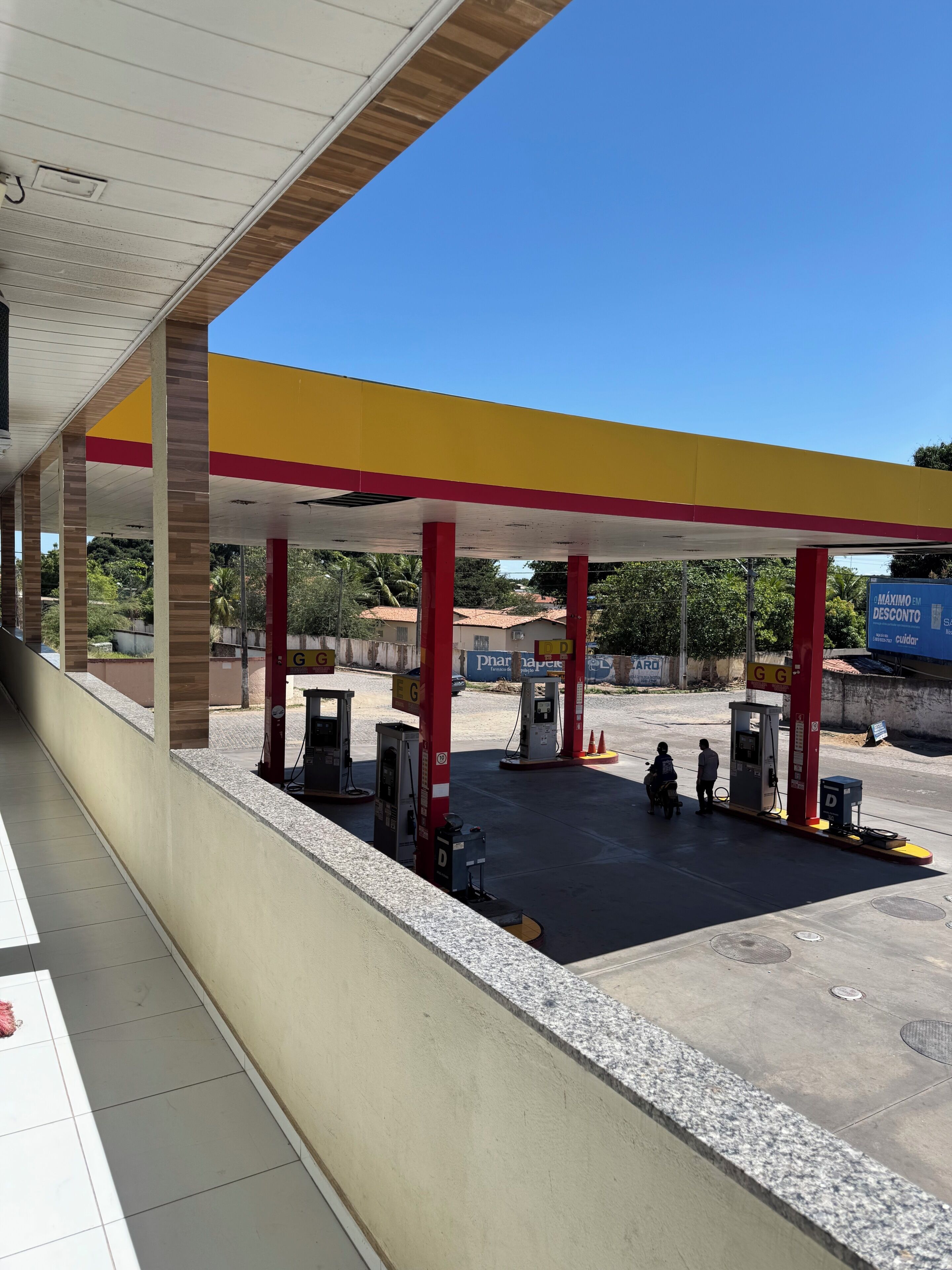 A gas station with multiple fuel pumps, a covered waiting area, and a clear blue sky.