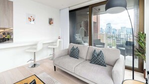 Una sala de estar moderna con un sofá, una zona de comedor y vistas a la ciudad a través de grandes ventanales.