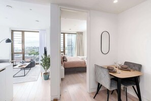 A modern apartment with a dining area, a bedroom with a large window, and a living space with a city view. - 16th Floor Skyline View | Balcony 2BR | Old Street (Greater London)