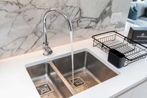 A modern kitchen sink with a chrome faucet, a marble backsplash, and a black dish rack on the countertop. - 16th Floor Skyline View | Balcony 2BR | Old Street (Greater London)