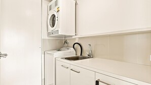 Cocina compacta con lavadora y secadora integradas, un lavamanos y grifo, y una puerta con manija.