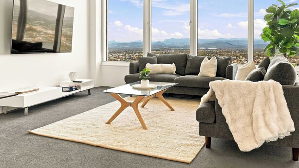 Un salón moderno con un ventanal grande, un sofá gris, una mesa de centro y un televisor montado en la pared.