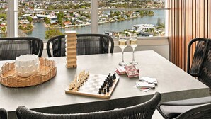 Un comedor con vistas a un río y un paisaje urbano, un juego de ajedrez, copas de vino blanco y una pila de libros.