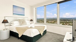 Un dormitorio con cama, dos lámparas de noche, un televisor y un ventanal con vista a la ciudad.