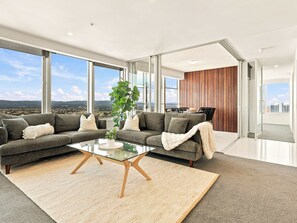 Een moderne woonkamer met een zithoek, een glazen salontafel en een groot raam met uitzicht op de stad.