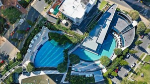 Vista aérea de un hotel moderno con piscina central, múltiples balcones y jardín ajardinado.