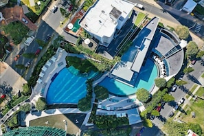 Ein Luftbild eines modernen Hotels mit einem zentralen Schwimmbad, mehreren Balkonen und einem angelegten Garten.
