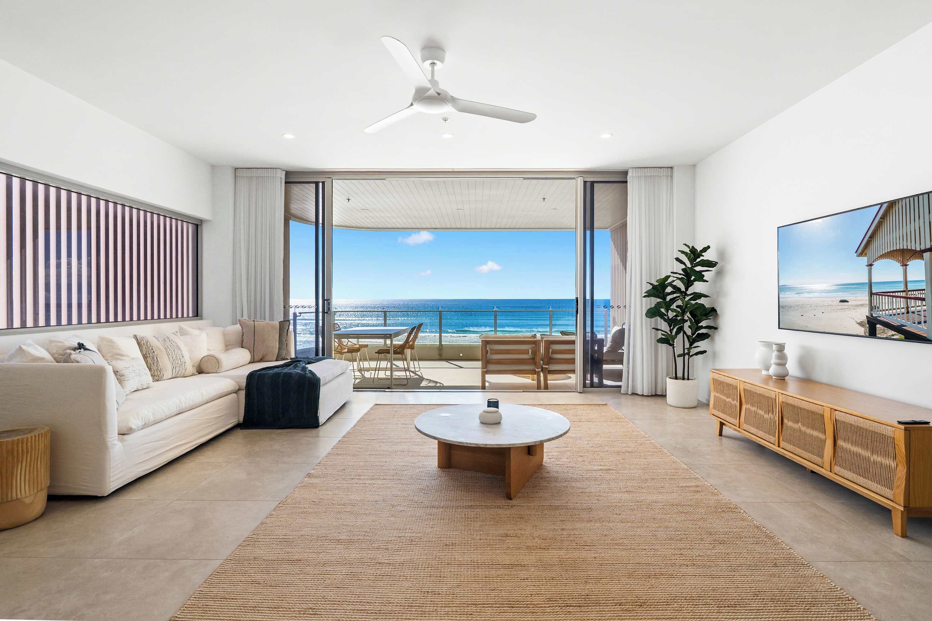 A spacious living room with a large window overlooking the ocean, a ceiling fan, and a modern interior design.